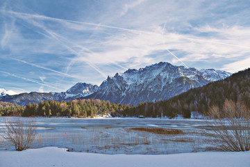 Zugefrorener Bergsee mit steilen Felswänden im Hintergrund und verschneiter Landschaft