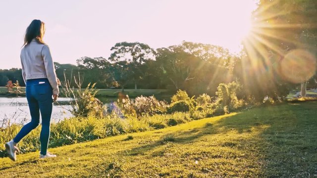 Fit girl walks along the shores of a lake at sunset appreciating its beauty