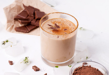 Lassi chocolate drink next to ice cubes, chocolate and cocoa on a white background
