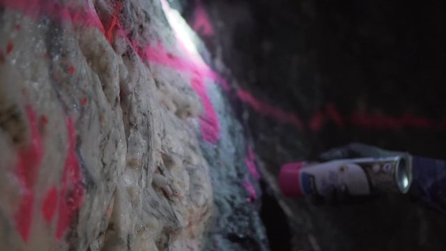 Underground person spraying pink paint onto gold bearing rock face