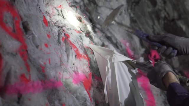 Person hammering quartz rock to collect a gold sample in underground mine site