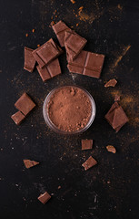 cocoa powder on a black background next to bars of chocolate and cinnamon.