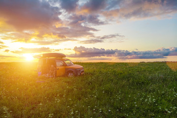 Couple sitting in a car in a green meadow at sunset.