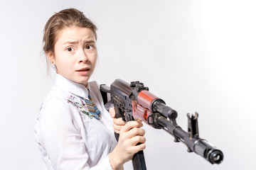 Girl with a frightened look with a Kalashnikov assault rifle in her hands on a white background in...