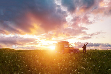 Fototapeta premium Man in a field with a raised hand near a car at sunset.
