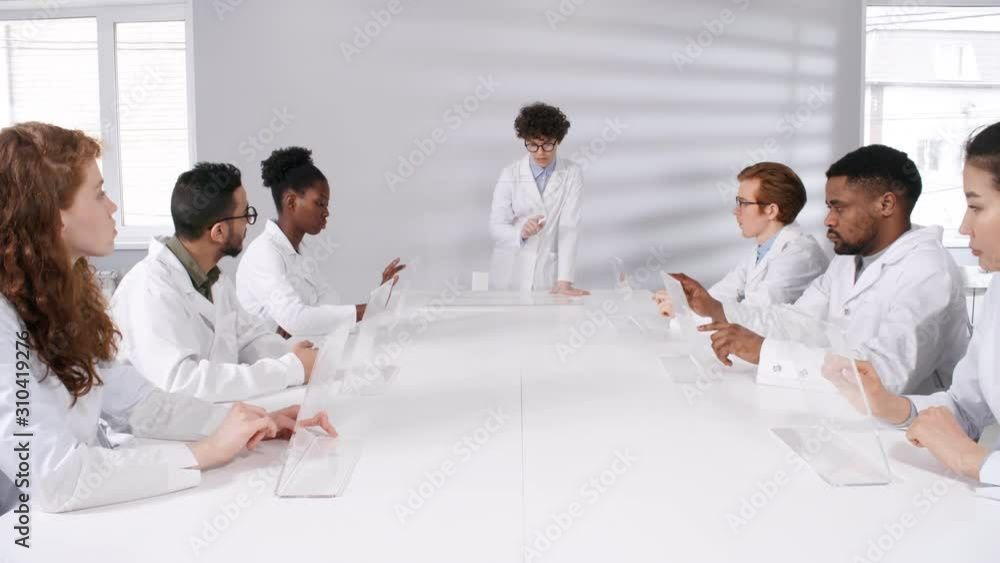 Poster waist-up shot of multinational students in lab coats sitting at table with interactive augmented rea