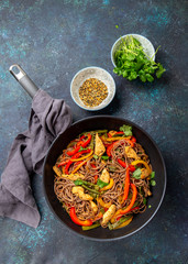 Japanese dish buckwheat soba noodles with chicken and vegetables carrot, bell pepper and green beans in wok on dark blue background