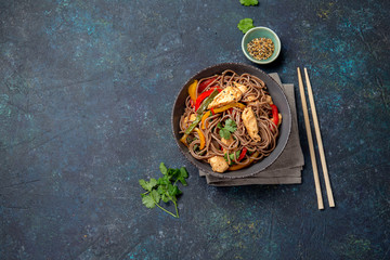 Japanese dish buckwheat soba noodles with chicken and vegetables carrot, bell pepper and green beans in grey bowl, top view, copy space