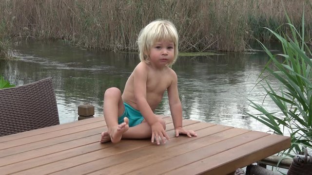Akyaka, Mugla, Turkey - 9th of November 2019: 4K Cute blonde toddle sits alone on table against river