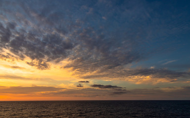 Naklejka na ściany i meble Sunset and dramatic set of clouds drifting over the tropical waters of the Caribbean Sea are lit by the last moments of daylight