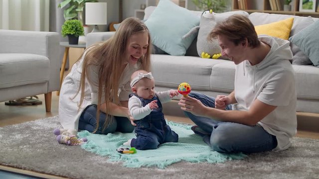 Little girl kid plays a rattle on the floor with parents