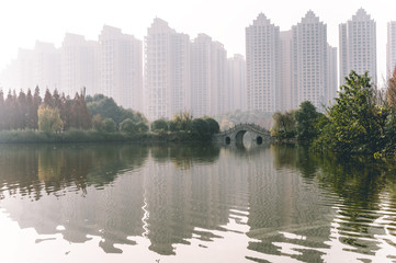 Fototapeta na wymiar The traditional Chinese architecture semicircle bridge over the Fuhe and Jiangan rivers in the Nanhu Wetland park of Chengdu, Sichuan, China. High-rise apartment buildings on background. Air pollution