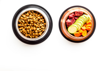 Healthy feed for cats and dogs. Bowls full of dry feed, meat and vegetables on white background top-down copy space