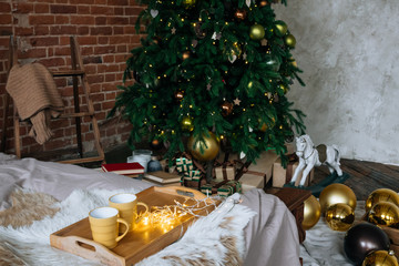 Cozy Christmas composition Two yellow mug with hot drinks on a wooden tray stand on the bed with a fluffy blanket against the background of Christmas tree in loft interior room in decor in garlands