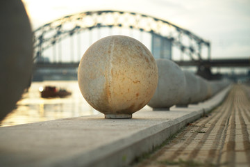 Closeup of stone balls decorating Daugava Promenade and tactile path for the blind in perspective, with the boat on Daugava river and Railway bridge in sunset light in the background