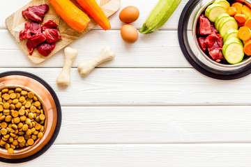 Ingredients of dry feed for dogs - meat, vegetables - near bones on white wooden background top-down copy space