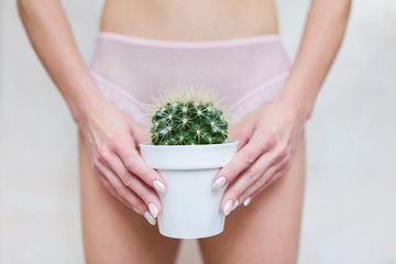 Depilation in the bikini zone concept. A woman holding a cactus in her hand staying in light pink...