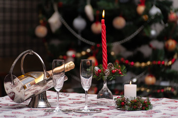 Naklejka premium Christmas or new year still life: decorated table with crystal shampagne glasses, wine bottle, candle and Christmas tree on the back