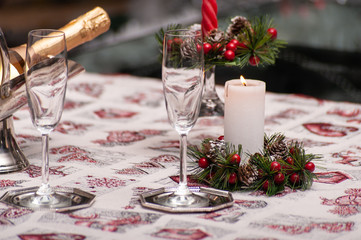 Christmas or new year still life: decorated table with crystal glasses, wine bottle, candle and Christmas tree on the back