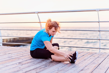 Woman with long blonde hair in blue shirt and black leggins doing stretching exercise deep side...