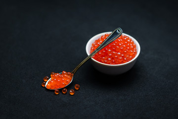 Red Caviar in a spoon. Caviar in bowl over black background. Close-up salmon caviar. Seafood. Delicatessen. Gourmet food. Texture of caviar. 