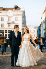 Lovely happy wedding couple, bride with long white dress posing in beautiful city