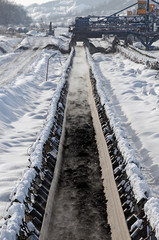 Coal on conveyor belt in winter conditions. Open-pit coal mine covered with snow.
