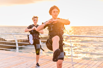 Women with her instructor training in EMS trainer on seaside at sunrise