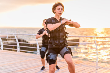 Women with her instructor training in EMS trainer on seaside at sunrise