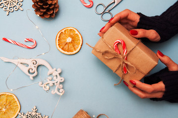 New Year flat lay with a gift in hand. A girl in a sweater holds a box with a bow in her hands on the background of Christmas decor
