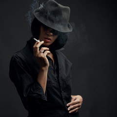 Girl brunette in black hat with cigarette on black background