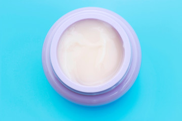 Jar with white cream on blue background, top view, copy space