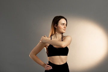 Athletic brunette girl in a black top kneading and doing exercises, on a gray background. Copy space