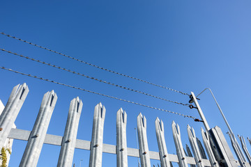 Sicherheitsbereich: Detailaufnahme Metallzaun mit Spitzen und Stacheldraht vor blauem Himmel