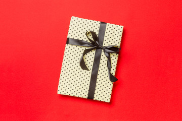 Gift box with black bow for Christmas or New Year day on red background, top view with copy space