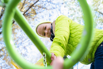 Smiling little girl in the park playing on playground outdoors autumn.