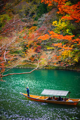 Fototapeta premium Boatman paddling the boat at Arashiyama forest view in the Autumn along Katsura river. Kyoto, Japan.