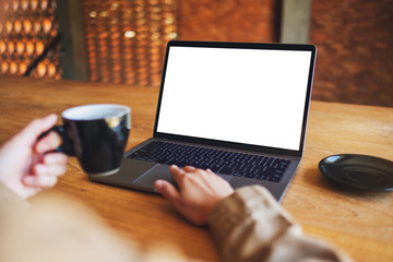 Fototapeta premium Mockup image of a woman using and touching on laptop touchpad with blank white desktop screen while drinking coffee