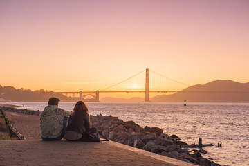 Beautiful Couple Sitting, Relaxing, Together at the Sunset with amazing view on Golden Gate Bridge in San Francisco, California, USA