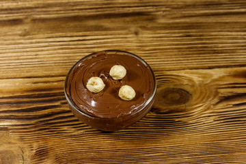 Glass bowl with delicious chocolate hazelnut spread on wooden table