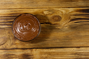 Glass bowl with delicious chocolate hazelnut spread on wooden table. Top view