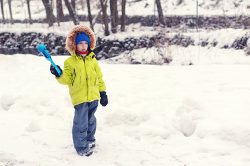 Fototapeta na wymiar Cute kid playing with snow in winter park. Little boy makes snowball with snowball maker