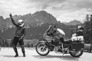 Fototapeta na wymiar Concept of destination. conquering the top, hand up, biker man dance happines. touring motorcycle on dirt road and mountains on background, tourism travel concept, copy space, black and white