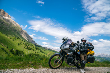 Motorcycle lady standing with adventure motorbike on the top mountain, enduro, off road, beautiful view, danger road in mountains, freedom, extreme vacation. Copy space. Passo Pordoi, Italy