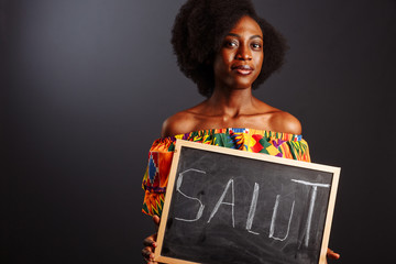 The portrait of young african woman student in clothes holding a chalkboard with a hello word in her own native language isolated on gray background