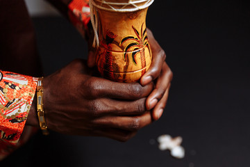 Hands of an African man in national clothes holds djembe drum surrounded by seashells