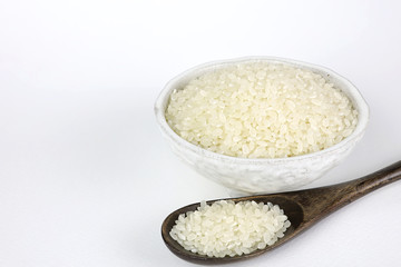 Japanese rice in a ceramic cup and wooden spoon on isolated white background.