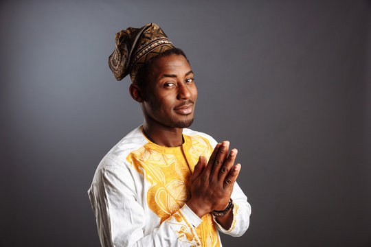 African Man In National Clothes And Traditional Headdress Gele From Nigeria Is Praying Before The Gray Wall