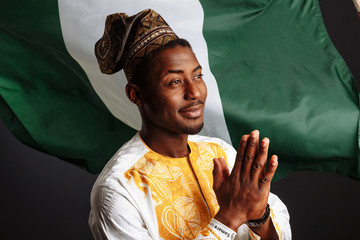 African man in national clothes and traditional headdress Gele from Nigeria is praying before the...