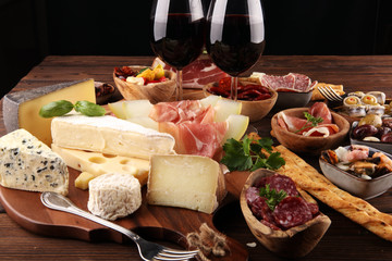 Italian antipasti wine snacks set. Cheese variety, Mediterranean olives, seafood salad, Prosciutto di Parma, tomatoes, anchovy and wine in glasses
